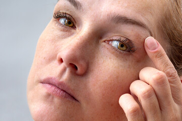 Middle aged caucasian woman of 40s holding fingers on eyelids to show eyes aging