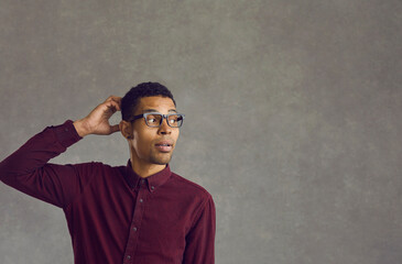 Questioning african american man with overwhelmed emotion on face scratching head look away nervously standing against grey background. Confused doubtful puzzled young black guy portrait - obrazy, fototapety, plakaty