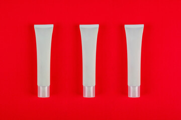 Plastic white tube for cream or lotion. Skin care or sunscreen cosmetic on red background.