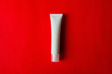 Plastic white tube for cream or lotion. Skin care or sunscreen cosmetic on red background.