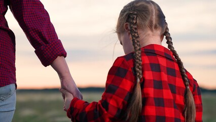 Daughter parent holding hands at sunset. Kid child mom woman mother strolling in field at sunrise....