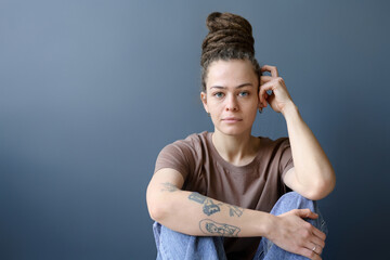 Minimal portrait of tattooed Caucasian woman with dreadlocks in bun hairstyle looking at camera...