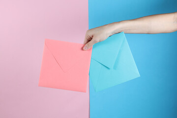 Female hand holding blue and pink envelopes on pastel background