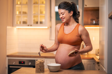 A healthy mid adult pregnant woman preparing cereal for breakfast in a kitchen