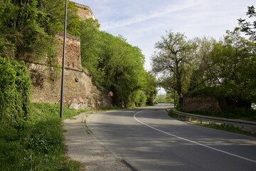 the road near the old fortress and green trees makes a smooth bend