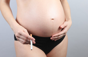 Bad habits during pregnancy. Pregnant mother holding a cigarette on a gray background