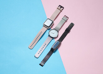Modern smart and analog watches and bracelet on a blue-pink background. Top view