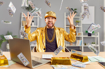 Successful excited young funny man in golden suit sitting at desk with gold bar, building online...
