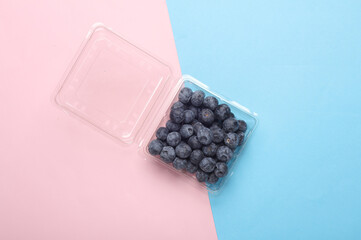 Blueberries in a transparent plastic box on a pink blue background. Top view