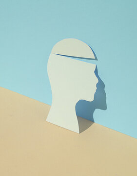 Paper-cut silhouette of a head on pastel background. Mental health