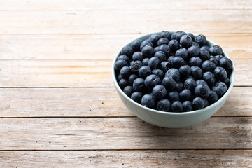 Blueberries in green bowl on wooden table. Copy space