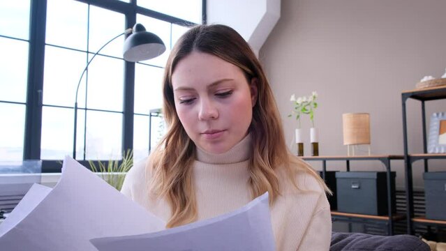 Concentrated Caucasian woman working online and talking to webcam on video call at home office. Businesswoman engaged in paperwork during online conference.