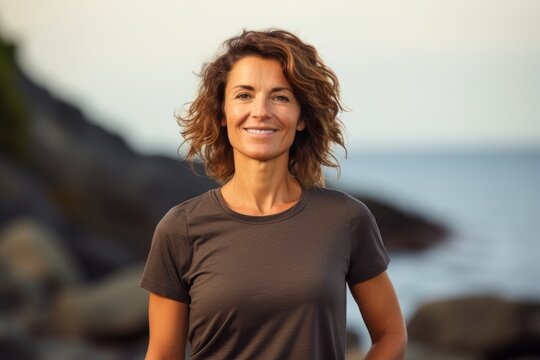 Portrait of a satisfied woman in her 40s dressed in a casual t-shirt over rocky shoreline background