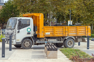 Fototapeta na wymiar White Truck With Yellow Tipper in City Park Works