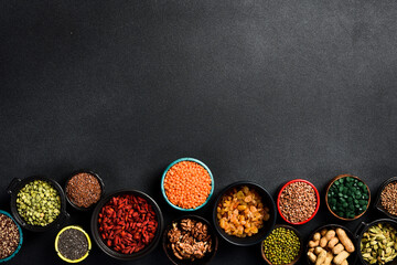 Superfoods and cereals selection in bowls: chia seeds, peas, green spirulina, goji berries and nuts, raisins, buckwheat, flax and quinoa. Free space for text.