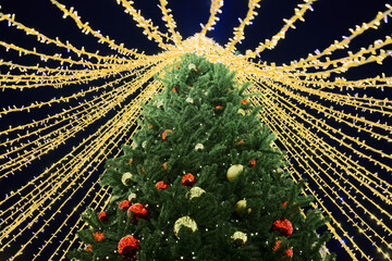 New Year christmas tree decorated Christmas balls with yellow flickering lights of garlands and white star topper on green tree at night, merry Christmas and happy New Year mood with twinkling lights
