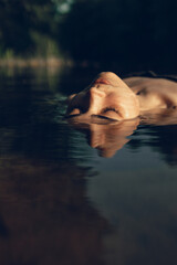 Woman with closed eyes lying in calm water of lake in summer 