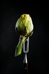Ripe organic artichoke on a metal fork. On a black background, vertical photo. - 788118417