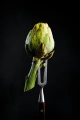  Ripe organic artichoke on a metal fork. On a black background, vertical photo. © Yaruniv-Studio