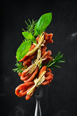 Smoked kabanos sausages with herbs. on a metal fork. On a black background, vertical photo. - 788118418