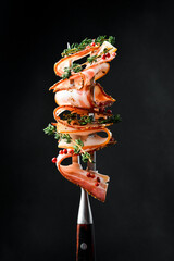 Slices of smoked bacon on a metal fork. On a black background, close-up. - 788118464