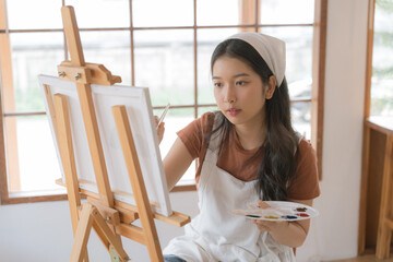 Asian young talented woman artist coloring on painting board in house. Attractive beautiful female draw art picture, creating artwork with watercolor paint and brush enjoy creativity activity at home