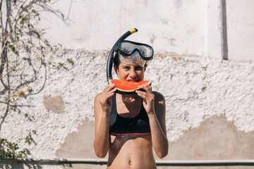 A girl is holding a watermelon slice in her mouth while wearing a snorkel, concept of fun and...