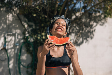 Teenage girl making a happy gesture while holding a slice of watermelon in her hands and wearing a...