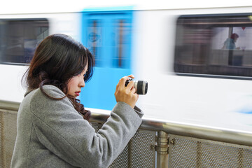 駅のプラットホームから電車を撮影する女性 - obrazy, fototapety, plakaty