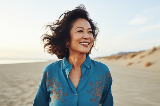 Portrait of a jovial asian woman in her 60s sporting a versatile denim shirt on serene dune landscape background