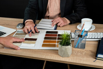 Designer hand choosing wood texture laminate  in catalog at office desk, laptop pen and notepad