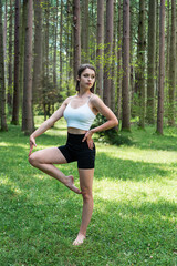 young caucasian woman in sportwear practicing yoga   on green grass in the park