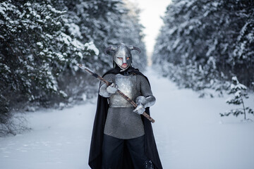 Portrait of a medieval fantasy warrior in a horned helmet, steel cuirass, chain mail with a two-handed ax in his hands, standing in a fighting position against the backdrop of a winter forest.