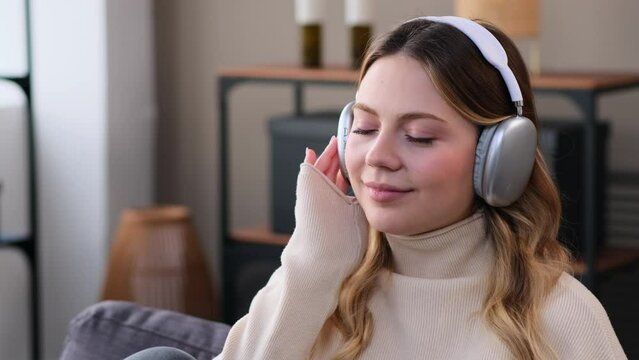 Happy Caucasian young woman listening music using headphones during weekend free time at home. Audio entertainment and pleasure concept.