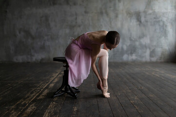 Ballerina sits on a chair and examines her pointe shoes