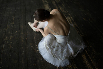 Ballerina in a white tutu sits on the floor and adjusts her pointe shoes