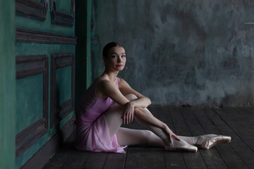 Portrait of a ballerina sitting on a wooden floor.