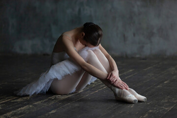 Tired ballerina sits on a wooden floor and rests.