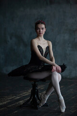 Portrait of a ballerina in a black suit sitting on a chair.