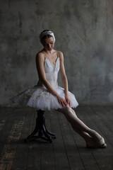 Portrait of a ballerina in a white suit sitting on a chair.