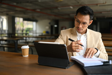 Asian businessman looking at digital tablet and checking financial documents at a cafeteria