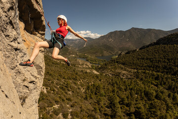 A woman is climbing a rock wall with a rope. The scene is set in a lush green forest with mountains...