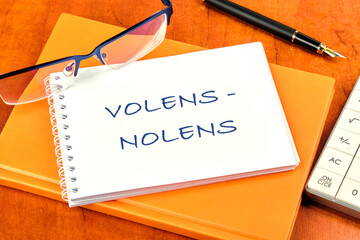 Willy - nilly latin expression volens-nolens (willing or unwilling) written on a clean white notebook