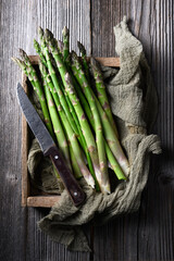 Fresh sprouts of picked asparagus in wooden box with knife and kitchen rug. Top view. Food photography