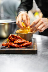 Person adding fries to a bowl beside crispy chicken wings on a wooden board, illustrating a delightful meal preparation
