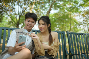 Young couple using mobile phone while sitting on a bench in urban park