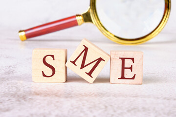 Wood SME on wooden cubes on an abstract background with a magnifying glass in the background