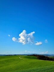 The lonely cloud in the blue sky and the lonely road on the green hill
