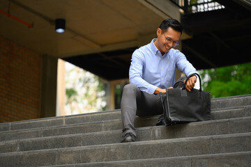 Full body shot of casual young businessman with briefcase sitting on stairs in the city