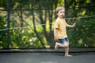 Cute little boy jumping on a trampoline in a backyard on warm and sunny summer day. Sports and...